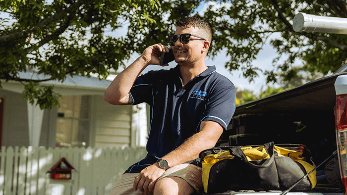 tradie sitting on the tray of a work vehicle and talking on the phone