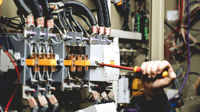 close up of tradies handing holding a red screwdriver working on switchboards for an HVAC system 