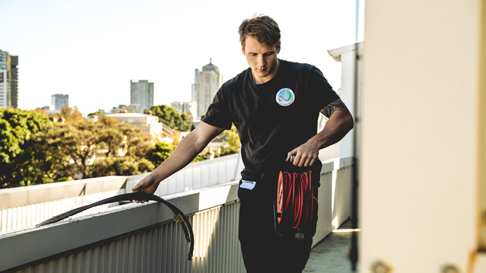 young tradie on the roof holding black piping in one hand and red extension cord in the other 