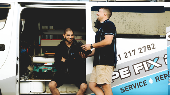 two tradies sitting on the side of company vehicle chatting and laughing