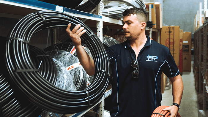 man grabbing a roll of black pipes in from store room