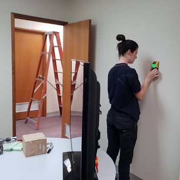 An electrician using a stud finder on a wall before hanging a television