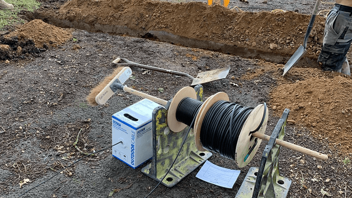 dirt ground with trench dug up and rolls of wiring next to trench 