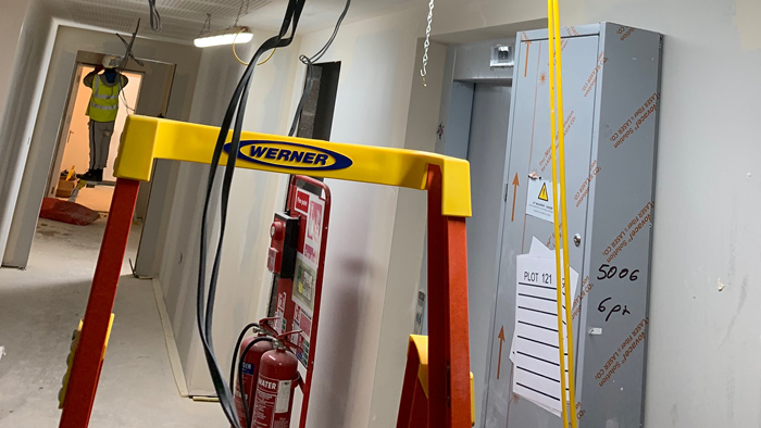 hallway with exposed wiring and man in far distant on ladder working