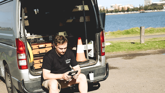 contractor sitting at the boot of company van looking at cellphone