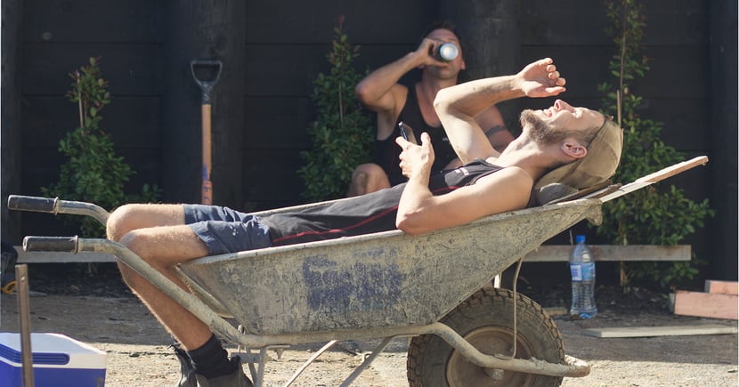 A landscaper lies in a dirty wheelbarrow, laughing